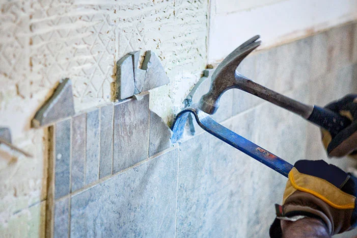 Person entfernt Fliesen mit Hammer und Meißel